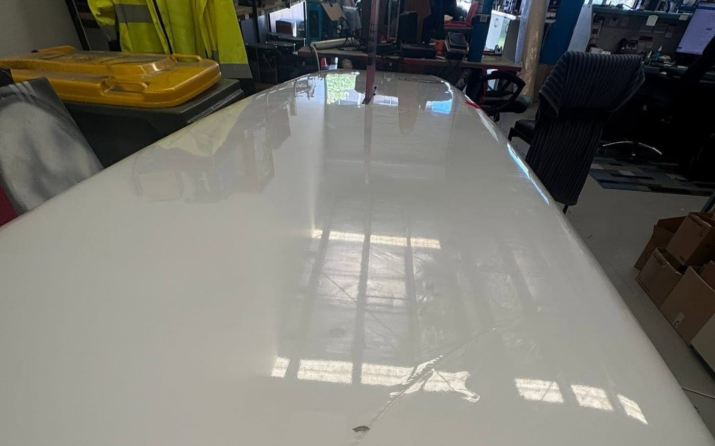 The finished surf ski deck in high-gloss white, reflecting the workshop lights after its repaint
